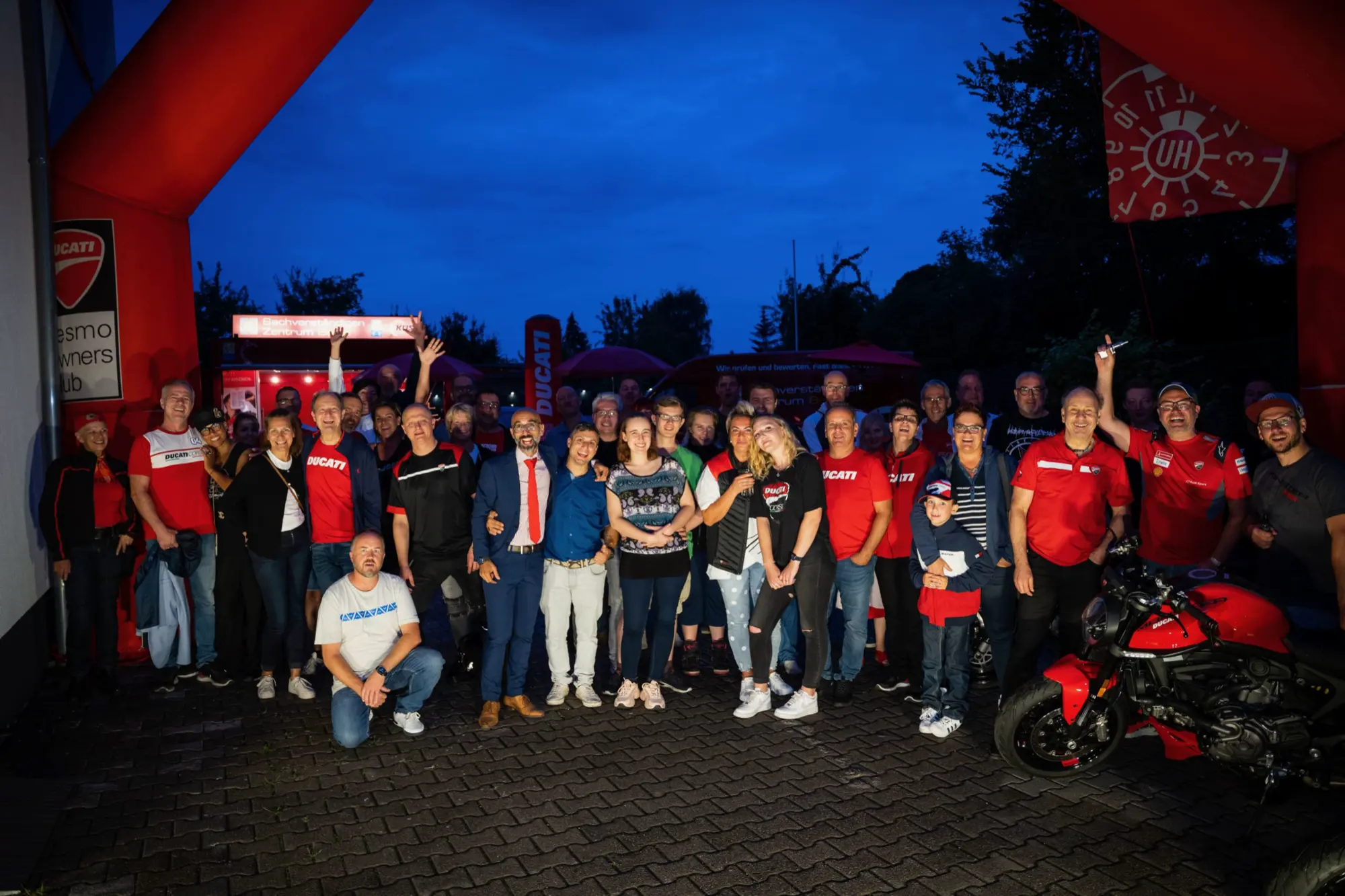 Gruppenfoto der Clubmitglieder am Abend unter einem Ducati-Torbogen