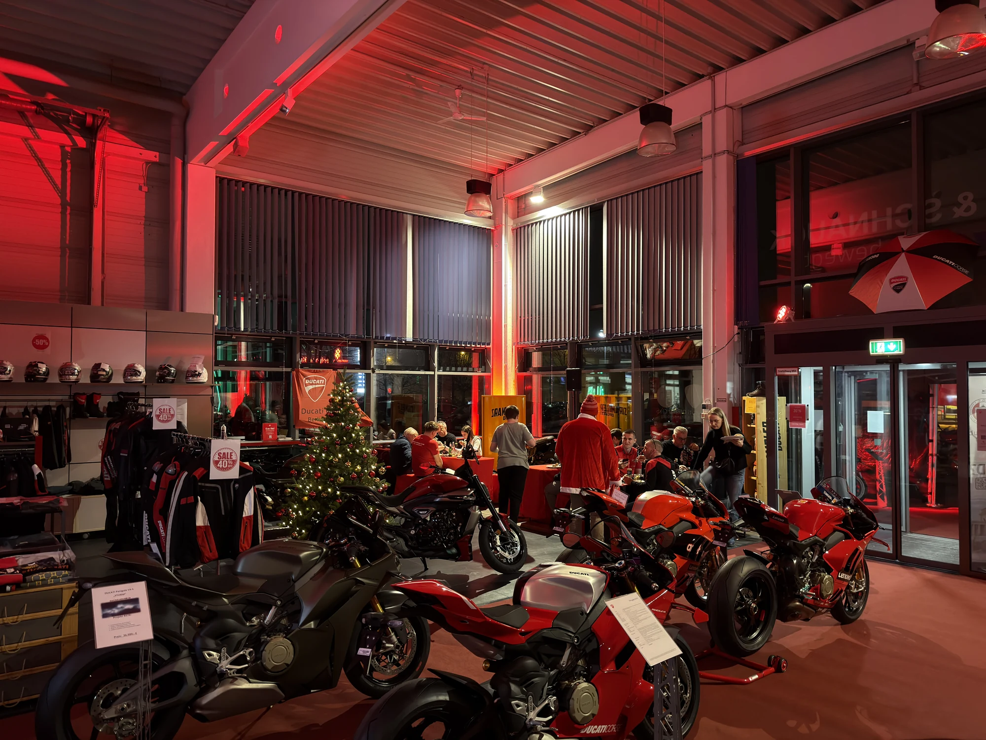 Weihnachtsfeier 2025 bei Riller & Schnauck: Ducati-Bikes und Weihnachtsbaum im rot beleuchteten Showroom